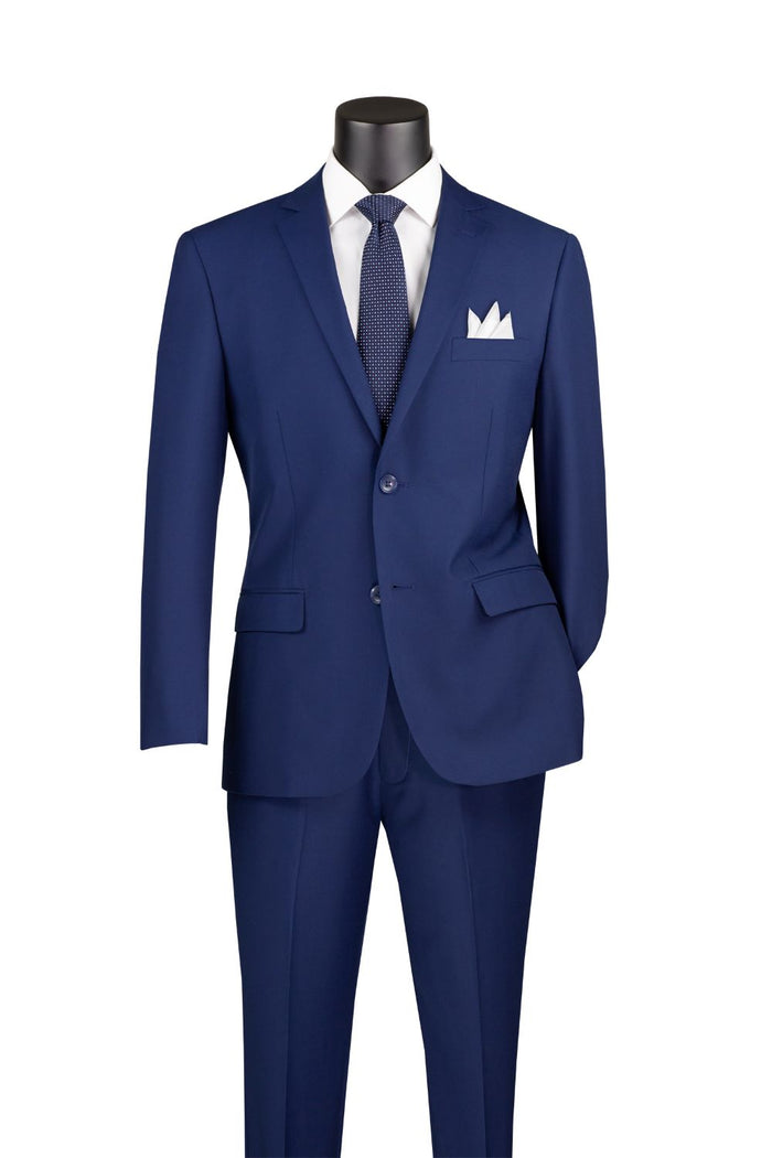 The Vinci Suits Slim Fit 2 Piece 2 Button Suit (Patriot Blue) SC900-12 features a notch lapel and is made from a wrinkle-resistant poly/rayon blend. It's displayed on a mannequin with a white dress shirt, coordinating blue tie, and crisp white pocket square.