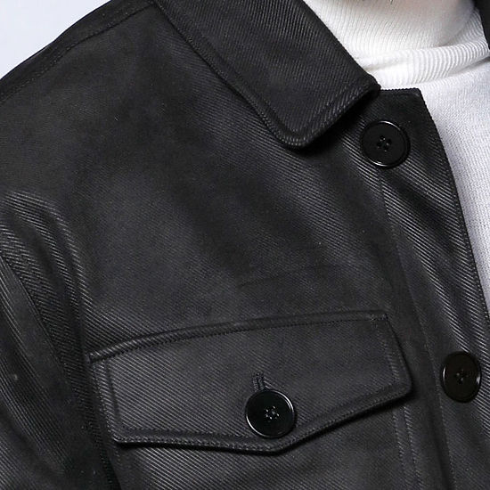 A man in a MANZINI SPAIN black large pockets button-up winter coat by Insomnia, made from refined poly blend fabric, stands over a white turtleneck against a white-paneled wall.