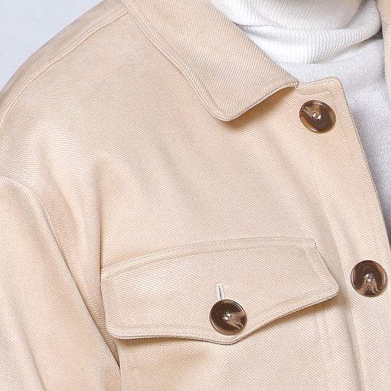 A man in a MANZINI SPAIN Tan Large Pockets & Button Winter Coat by Insomnia, layered over a white turtleneck sweater, stands elegantly against a light gray ornate background.