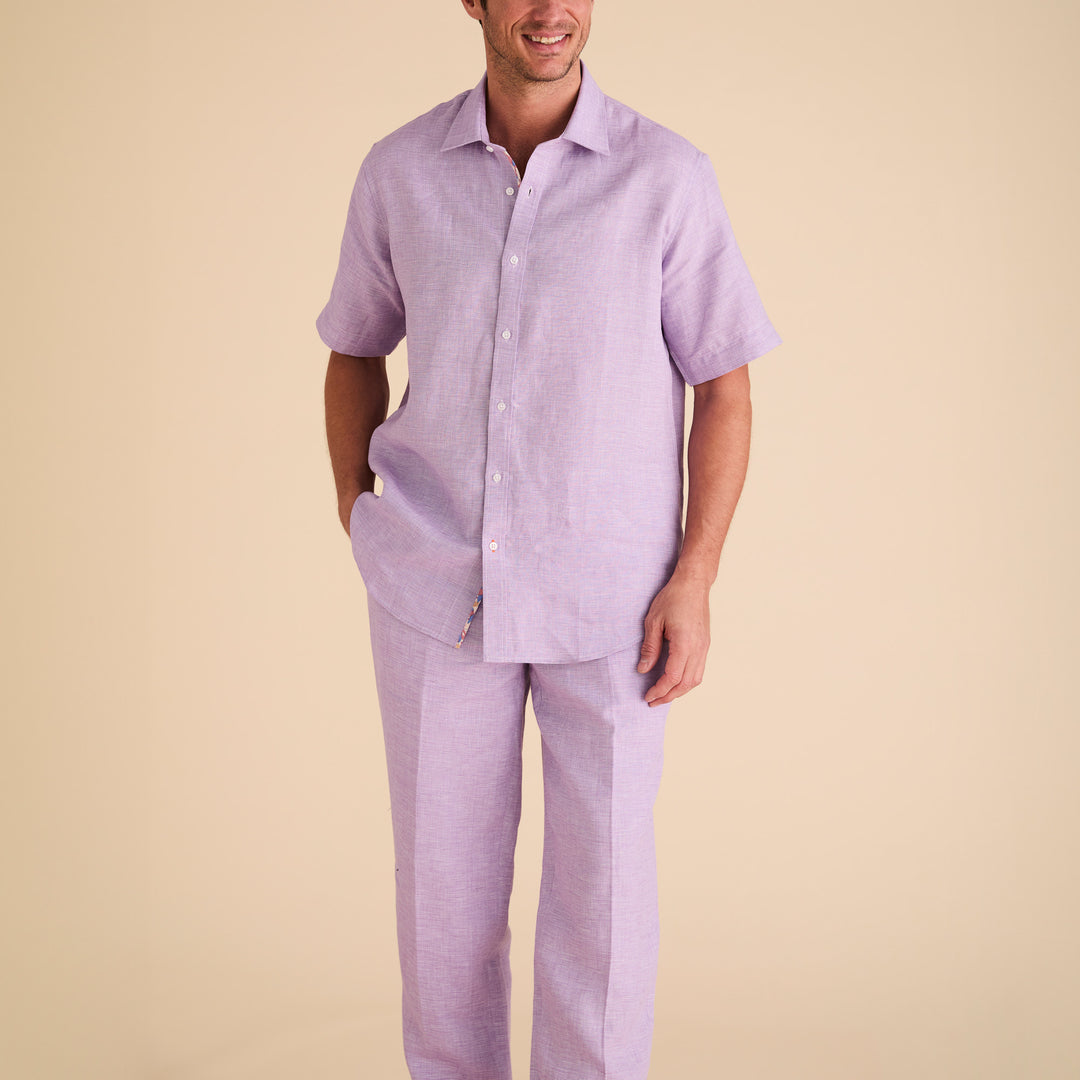 Man wearing an Inserch SS Linen Shirt SS717-00119 in lavender, short-sleeved button-up style, with matching pants, stands against a plain beige background.