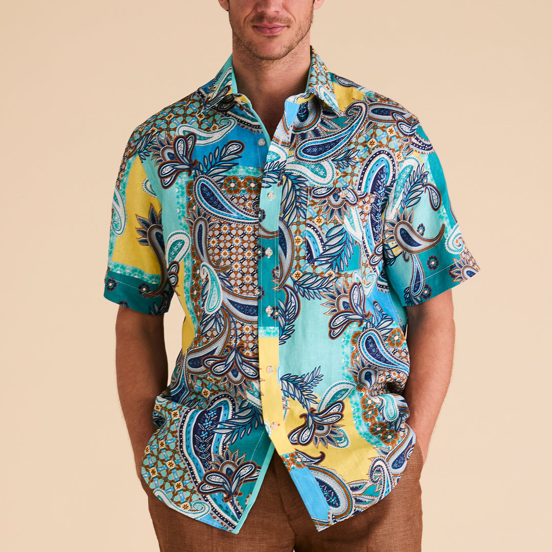 Someone is wearing the Inserch SS Mediterranean Paisley Print Linen Shirt in vibrant blue and yellow with pearlized buttons, standing against a plain background.