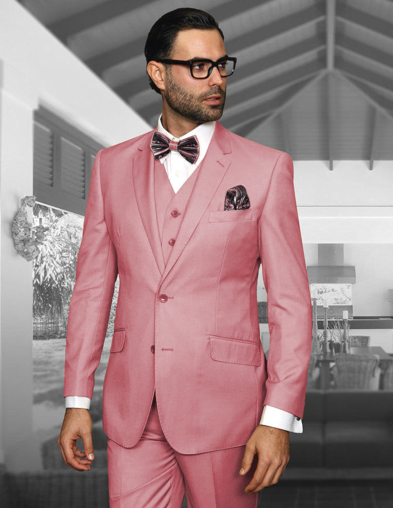 A man in the STATEMENT CLOTHING | STZV-102-BLUSH suit by Statement Clothing stands indoors, wearing a bow tie and glasses, looking to the side.