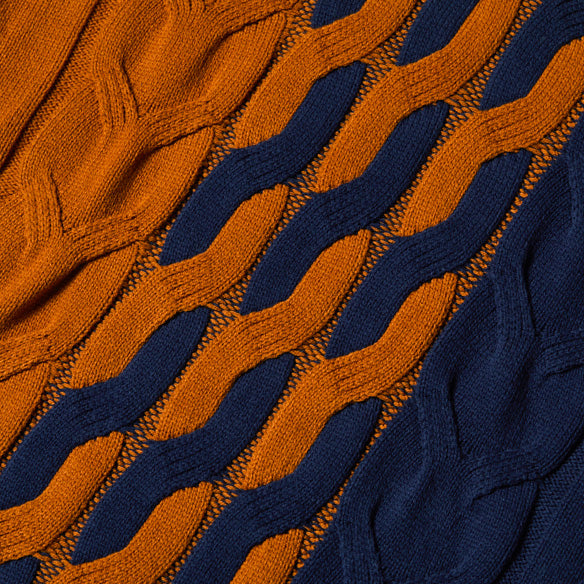 A man faces the camera, hands in pockets, wearing the Inserch Cotton Blend Cable Knit Turtleneck Sweater SW303-11 in navy by Inserch, featuring a colorblock design with orange and navy blue patterns.