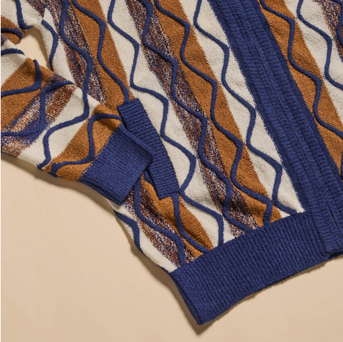 Man wearing the Inserch Bouclé Yarn Graphic Full Zip Sweater SW614-00001 Royal Blue, styled with a white turtleneck and brown corduroy pants against a beige background.