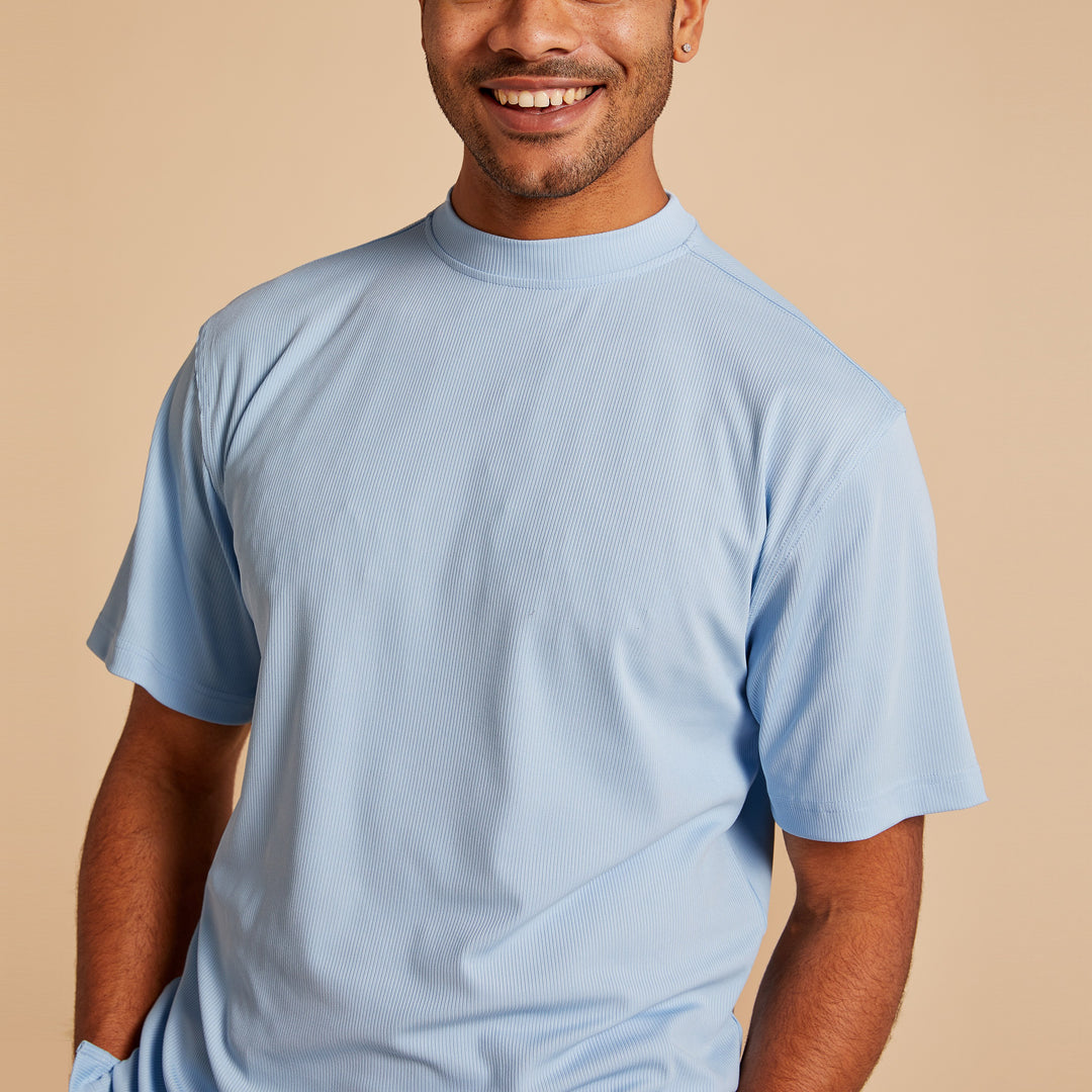 A person wearing the Inserch Rib Crew Neck T-Shirt T299-00154 Lake Blue by Inserch stands against a beige background, smiling with one hand in their pocket.
