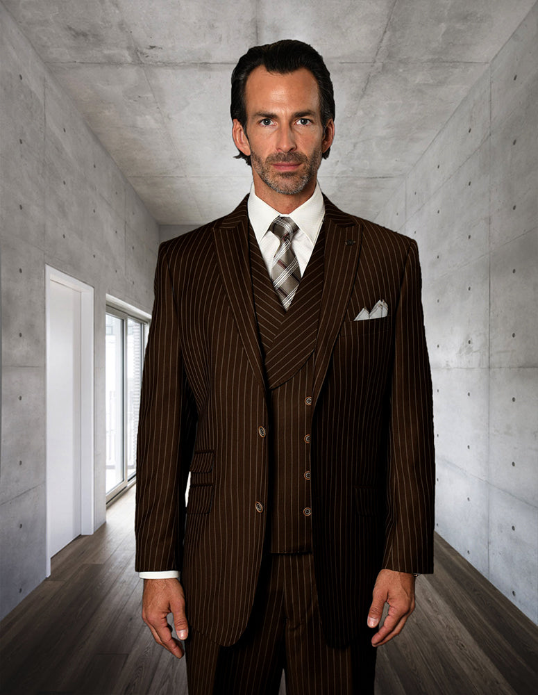 A man wears the STATEMENT CLOTHING | ZARELLI-BROWN pinstripe suit with pleated pants by Statement Clothing, standing in a sleek concrete hallway with wooden floors and a window on the left.