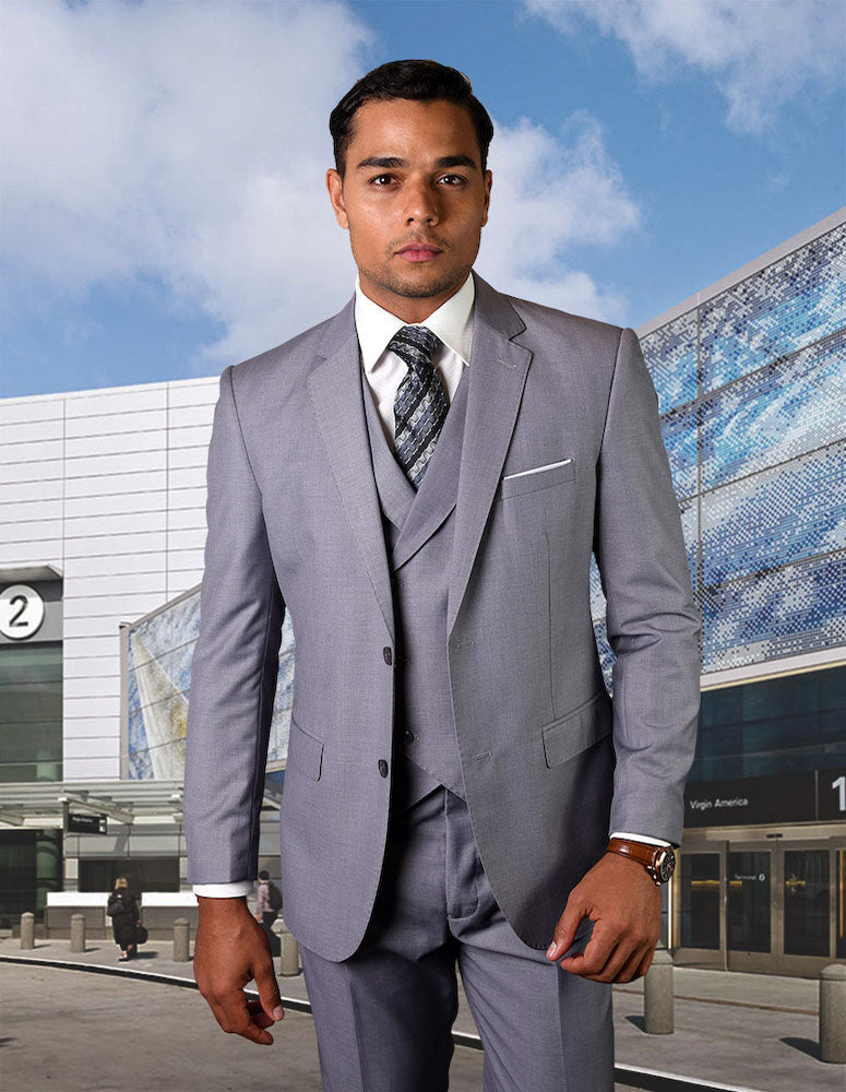 A man stands outside a glass-paneled building with the number 2 behind him, wearing Statement Clothing's STATEMENT CLOTHING | ZARGALA-GREY modern fit light gray suit, white shirt, and patterned tie.