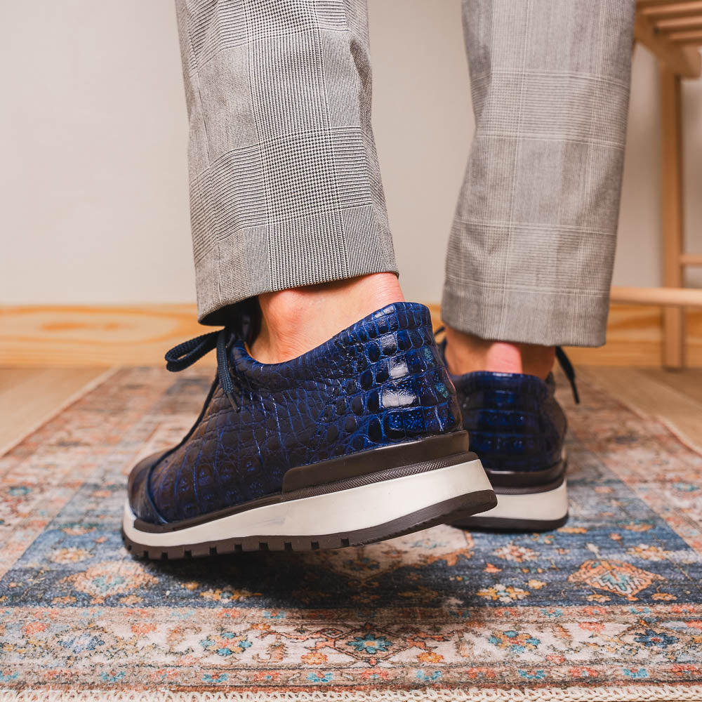 The Alonzo Navy by Marco Di Milano is a luxury men's sneaker in genuine caiman crocodile leather, featuring black laces, a hand-painted finish, white midsole, and black textured outsole.