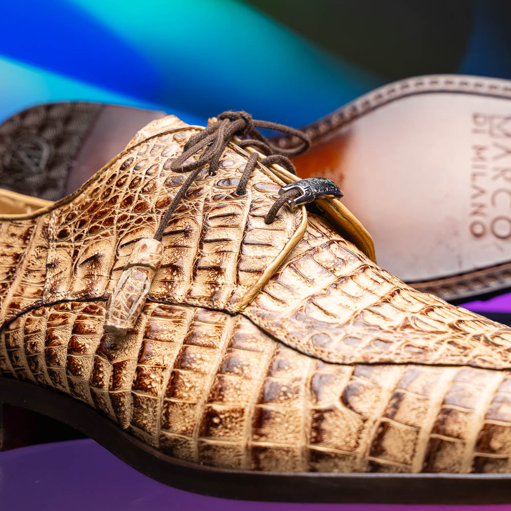 A pair of Marco Di Milano Apricena Rustic Orix luxury dress shoes in beige crocodile pattern, one upright and one on its side revealing the brown sole with embossed branding. Made from genuine caiman crocodile leather for an elegant finish.