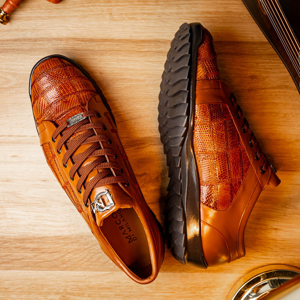 The Marco Di Milano Bari Cognac features brown leather with a hand-painted finish, textured side panels, black laces, and black rubber soles—one shoe propped against the other.