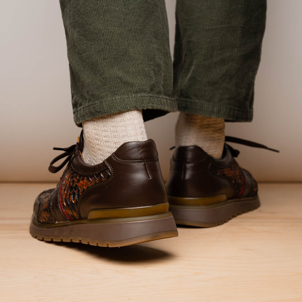 The Marco Di Milano Brescia Washed Cognac sneakers feature brown leather with a snakeskin pattern, gold accents, and rubber soles; one shoe is propped stylishly against the other, showcasing luxury footwear appeal.