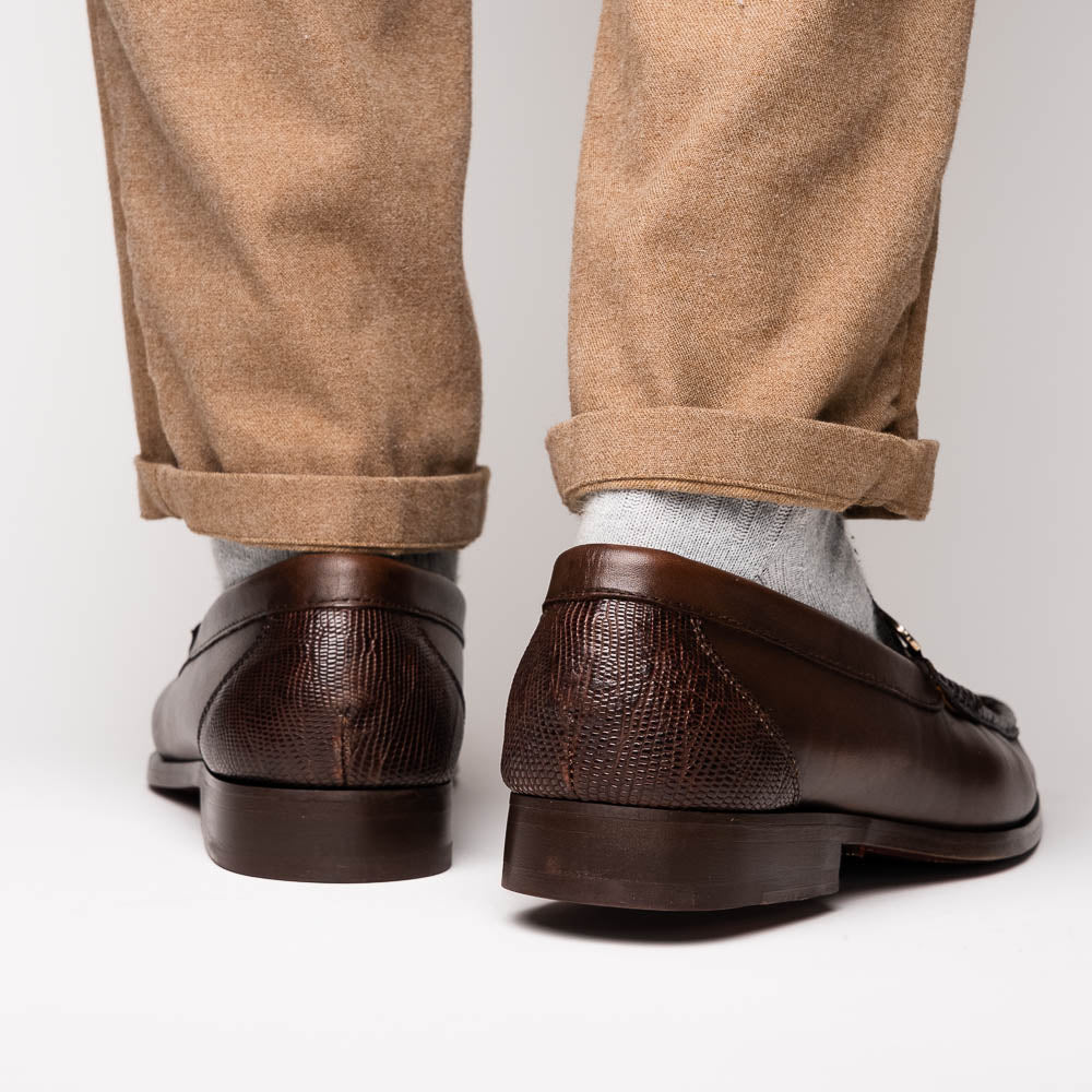 The Enzo Brown by Marco Di Milano features dark brown genuine lizard loafers with textured uppers, a metal buckle, and branded soles—luxurious men's footwear displayed against a white background.