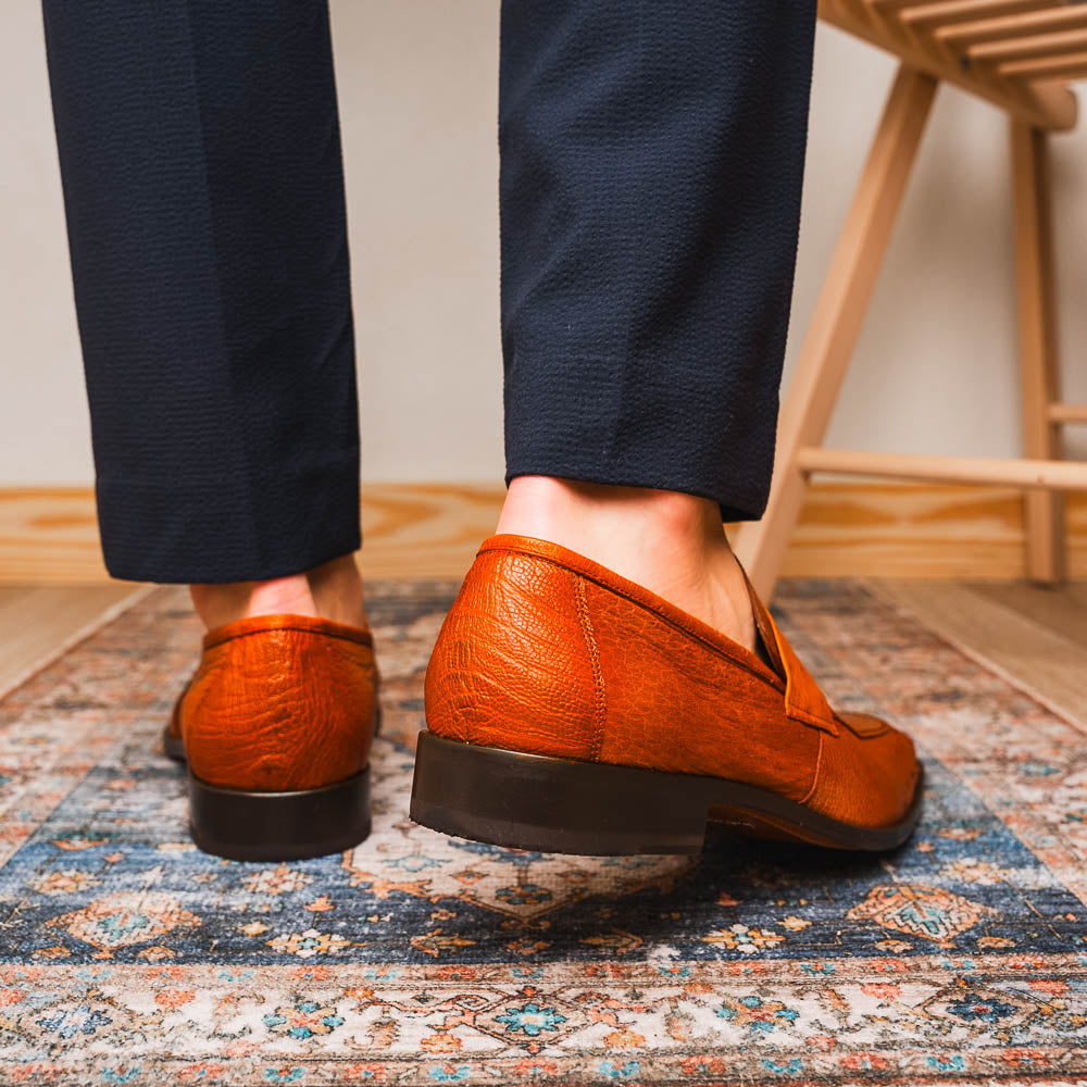 A pair of Marco Di Milano Fangio Cognac men's shoes in brown leather with textured detailing; one genuine ostrich loafer stands upright, while the other lies on its side showing the sole embossed with the brand name.