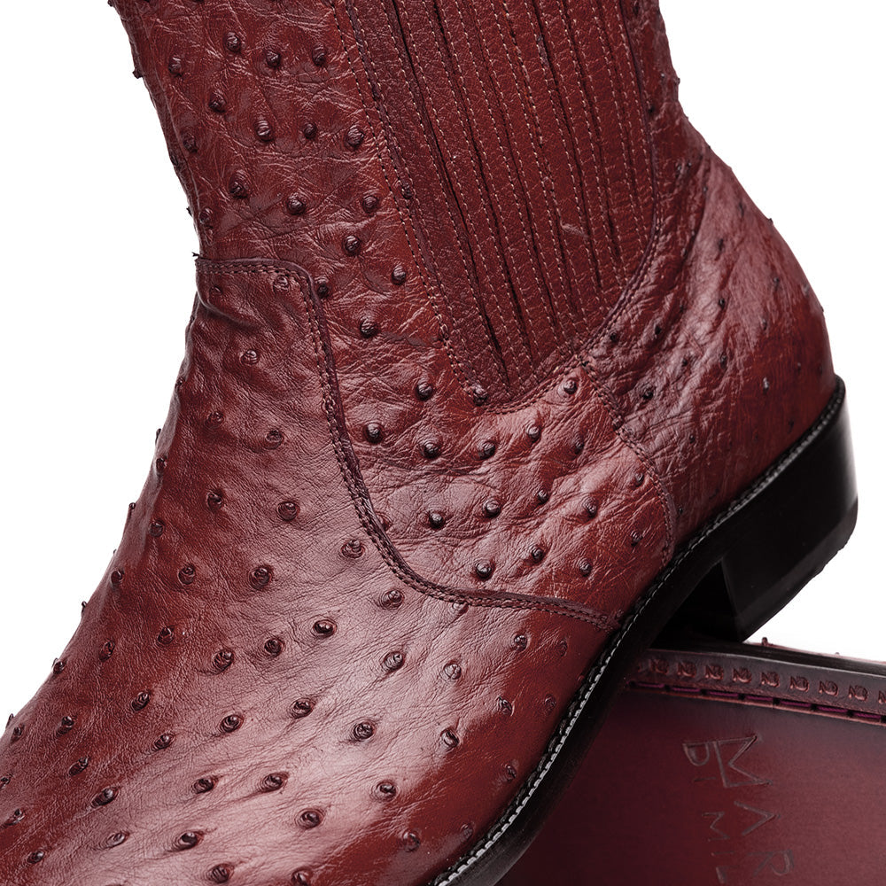 Introducing Giorgio Wine by Marco Di Milano: a pair of luxurious men's boots handcrafted in genuine burgundy ostrich leather, featuring a distinctive textured pattern, side zipper, elastic panel, and a sleek black sole—sophisticatedly presented against a white background.