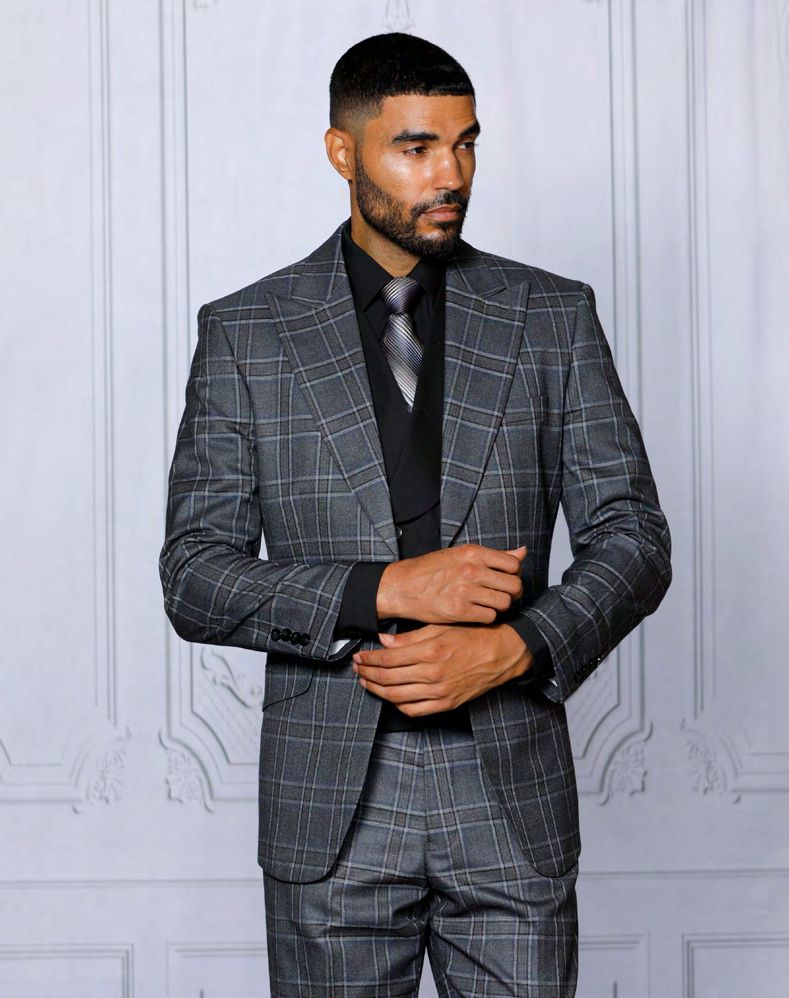 A man in an INSOMNIA PARIS-2 3PC Tailored fit Charcoal Suit by Insomnia, paired with a black shirt and tie, stands against a light-colored, textured wall, adjusting his outfit.