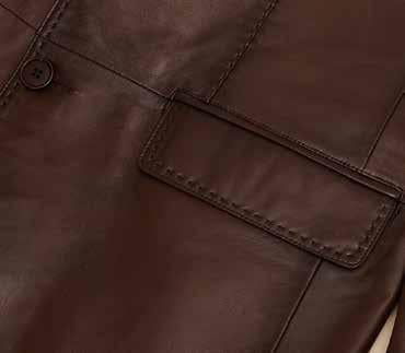 A man wearing the Inserch Lamb Leather Blazer 600-133 / 104 Cognac with a printed lining and plaid, regular-fit pants stands against a plain background, looking downward.