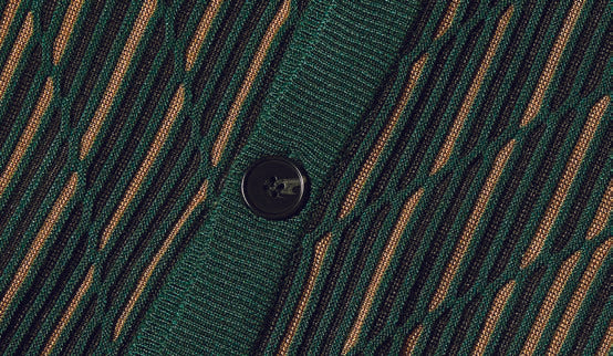 An individual is dressed in the Inserch Intarsia Panel Cardigan SW904-200 Emerald, featuring a geometric intarsia pattern over a tan turtleneck, complemented by brown corduroy pants, standing against a plain background.