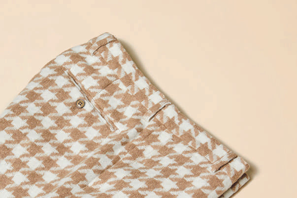 A person wearing Inserch Houndstooth Pants (P264-09 Khaki) in a modern fit, with a brown and white wool-blend houndstooth pattern, has their hands in pockets while paired with white sneakers and stands against a beige background.