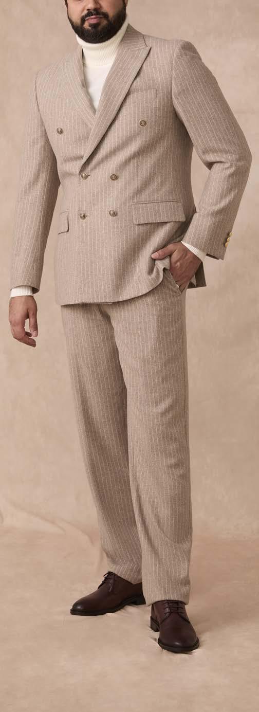 A man wearing the Inserch Wool Blend Flannel DB Stripe Suit (Stone) by Inserch, paired with a white turtleneck sweater and brown dress shoes, stands against a neutral background.