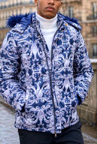 A man wears an Insomnia MZW-410 Soft Padded Poly Zip-up Jacket w/ Removable Navy Faux Fur Hood in blue with a white and blue ornamental pattern over a white turtleneck sweater.