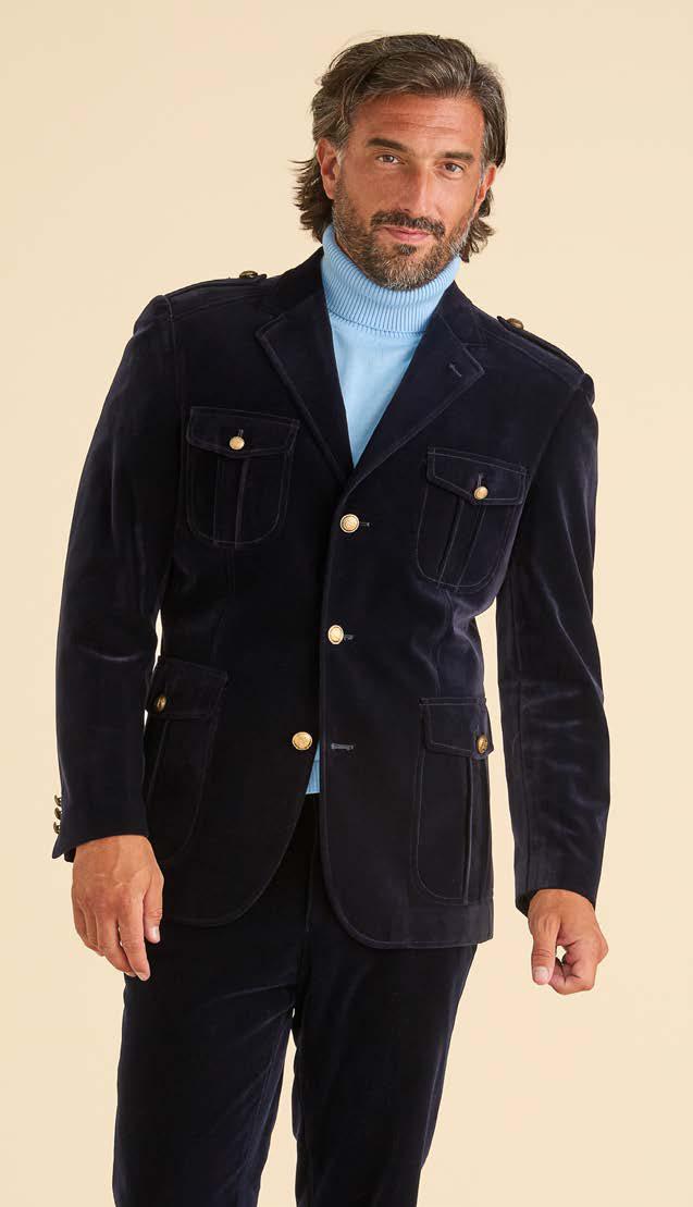 A man wearing the Inserch Velvet Military Blazer BL569-00011 in navy blue by Inserch, featuring jacquard lining and gold military shank buttons, paired with a blue turtleneck sweater and matching navy pants, stands against a plain light background.