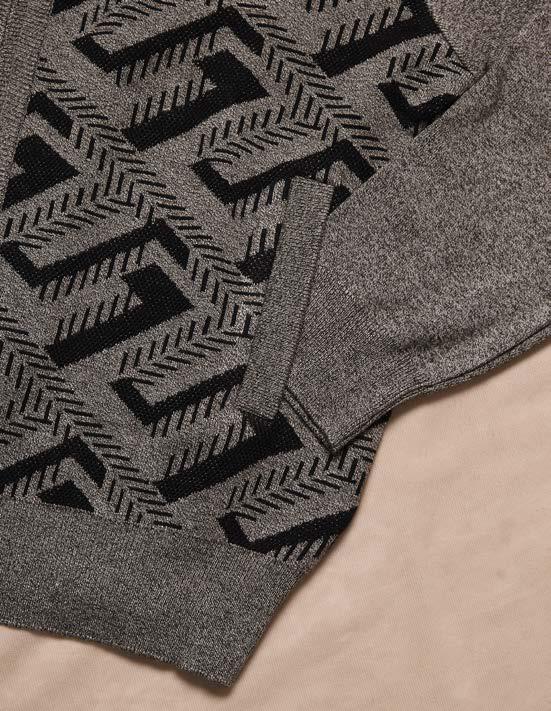 A man wearing the Inserch Full Zip Sweater SW616-00033 Grey, featuring a black geometric pattern, paired with black pants, stands against a beige background.