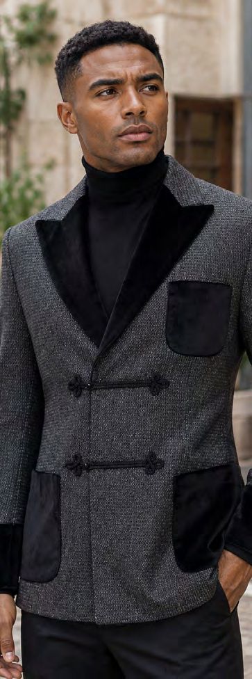 A man wears an Insomnia MANZINI MZW-556 Fancy Velvet Trim Sport Coat in charcoal, featuring a tailored fit, textured fabric, black velvet trim, pockets, toggle closures, and a black turtleneck.