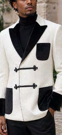 A man wears an Insomnia MANZINI MZW-556 Fancy Velvet Trim Sport Coat in a white tailored fit with black velvet lapels, cuffs, and pockets, featuring two toggle closures over a black turtleneck.