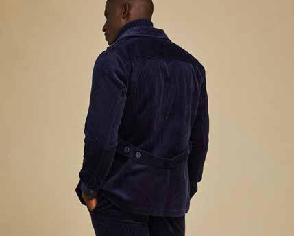 A person wearing the Inserch 4-Pocket Cord Jacket BL267-11 in navy, crafted from modern corduroy fabric made of 100% cotton, paired with an orange and blue patterned sweater underneath. Their hands are in their pockets against a beige background.