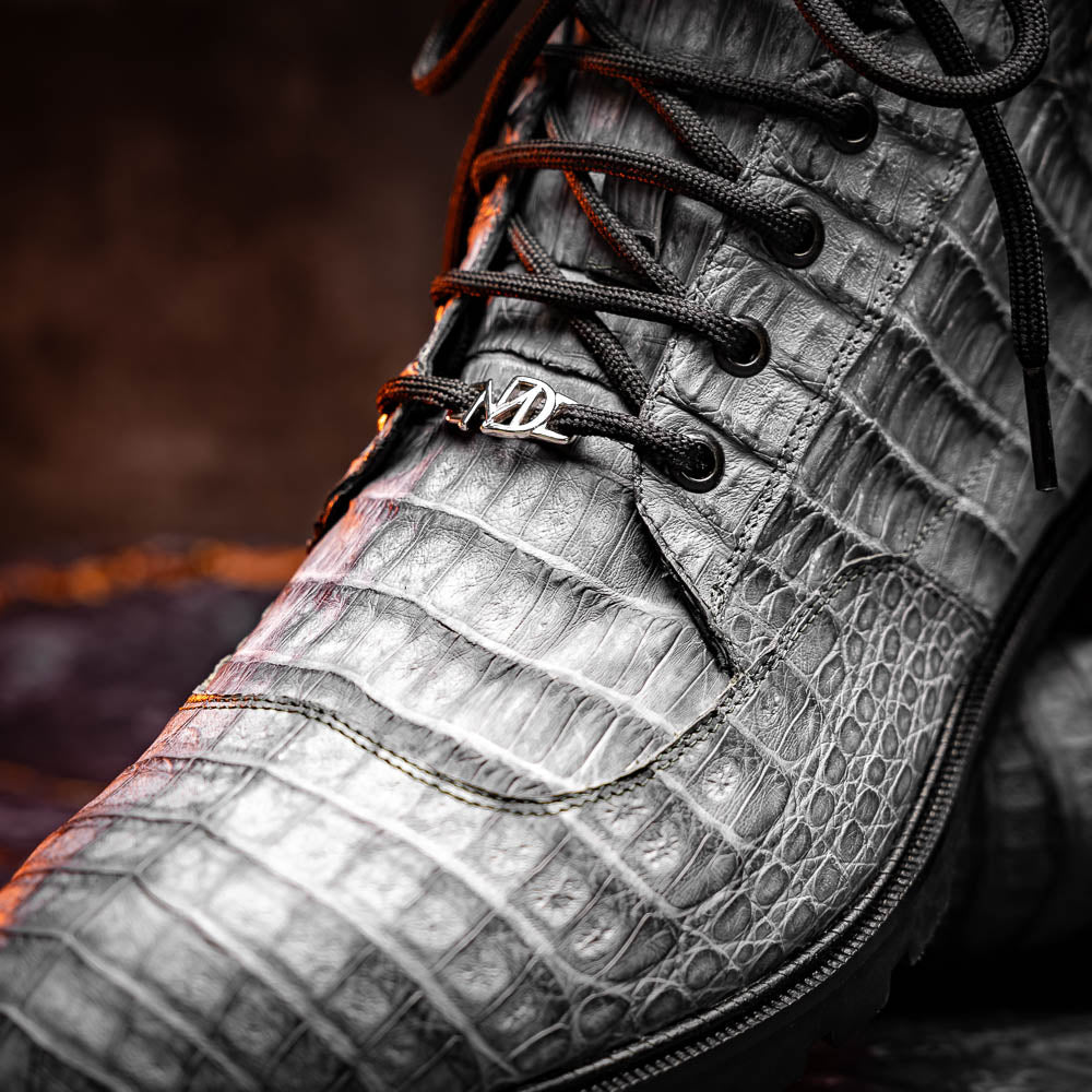 The Leoni Oil Gray boot by Marco Di Milano features a gray, crocodile-patterned design in genuine caiman leather with black laces, a thick rugged sole, and hand-painted finishes—all showcased on a white background.