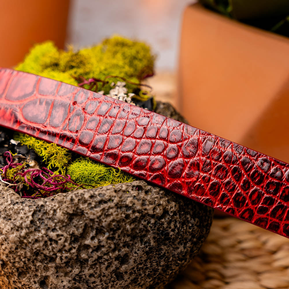 The Emilio Belt Antique Red by Marco Di Milano is a rolled-up red crocodile-patterned leather belt with hand-painted finishes and a silver buckle, displayed on a white background.