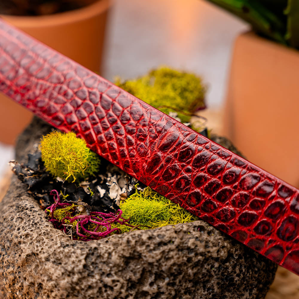 The Riccardo Belt Antique Red by Marco Di Milano is a rolled, red caiman belly belt with a crocodile pattern and a silver buckle engraved with the brand logo—an exceptional choice in luxury exotic belts.