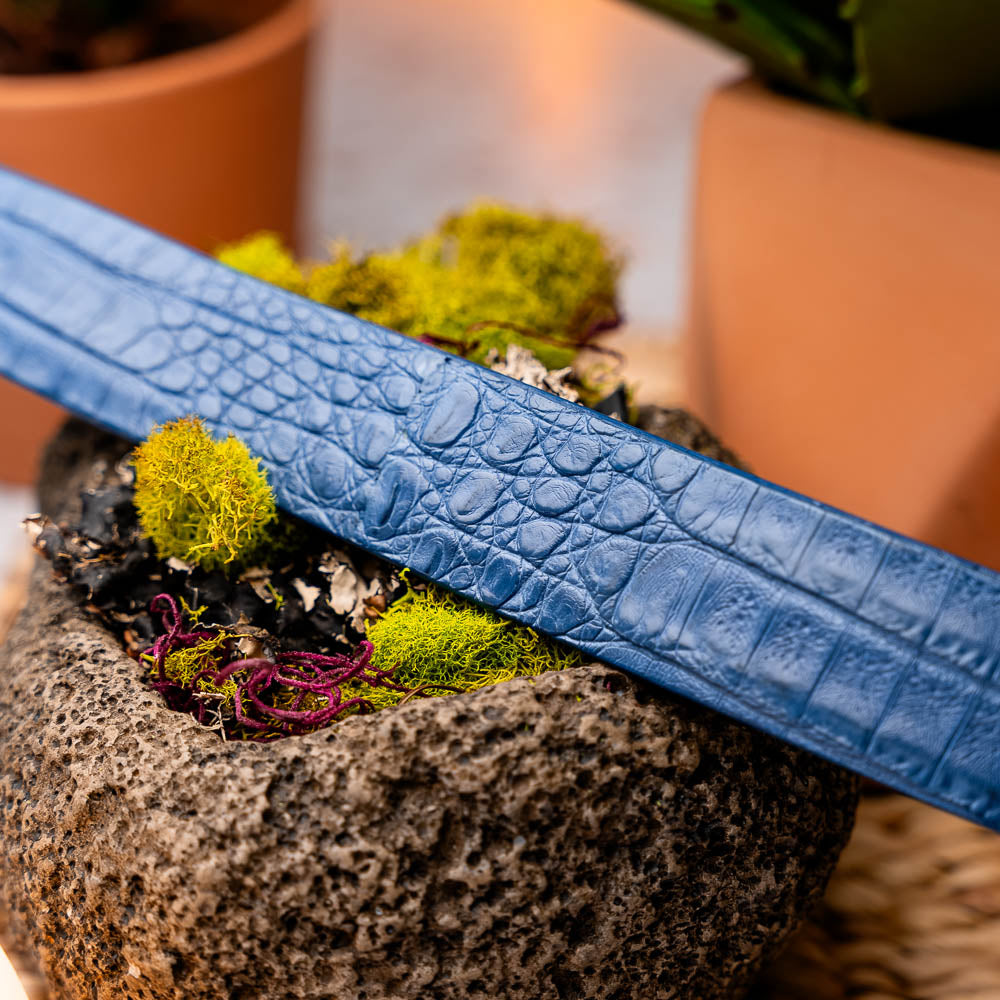 The Riccardo Belt Blue by Marco Di Milano features a caiman fuscus belly with crocodile pattern and a silver buckle engraved with "Marco Di Milano" and "MDM," making it ideal to pair with luxury footwear.