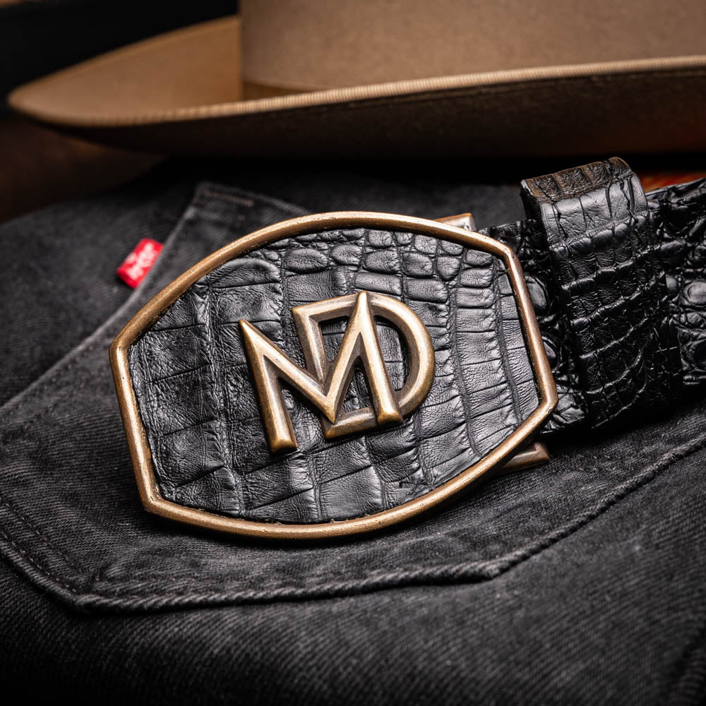 The Marlboro Belt Black by Marco Di Milano features textured hornback caiman leather and a gold buckle with stylized "MD" initials, displayed against a white background.