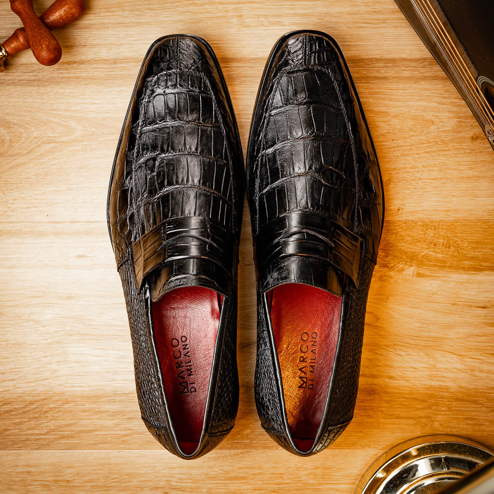 The Matteo Black by Marco Di Milano is a pair of black genuine alligator slip-on shoes with a polished brown leather sole, embossed branding, and hand-painted finishes, shown against a white background.