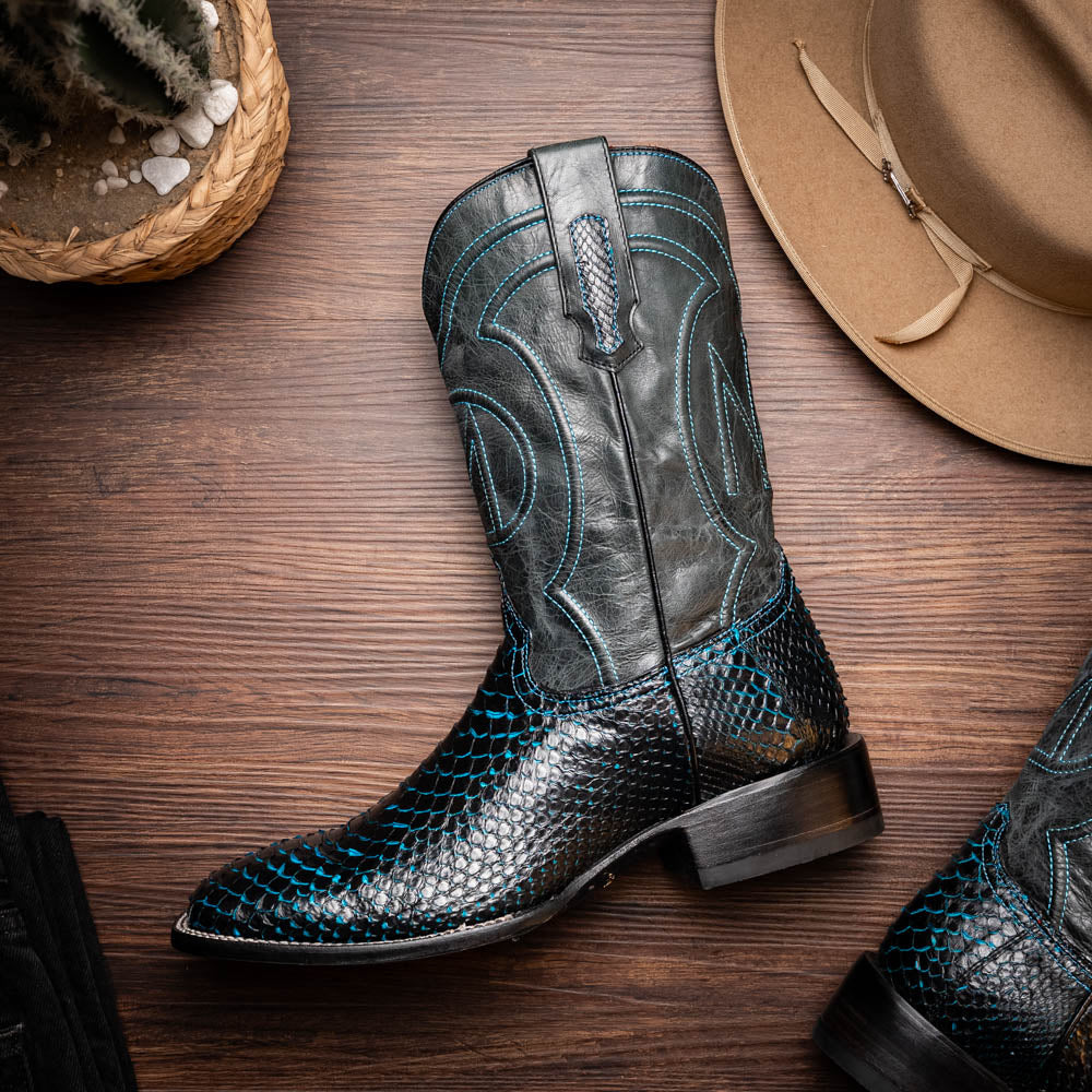 The Missouri Black / Blue boots by Marco Di Milano are handcrafted men's cowboy boots in black and blue, featuring genuine python skin and a textured snakeskin pattern—one boot upright, the other revealing the branded sole.