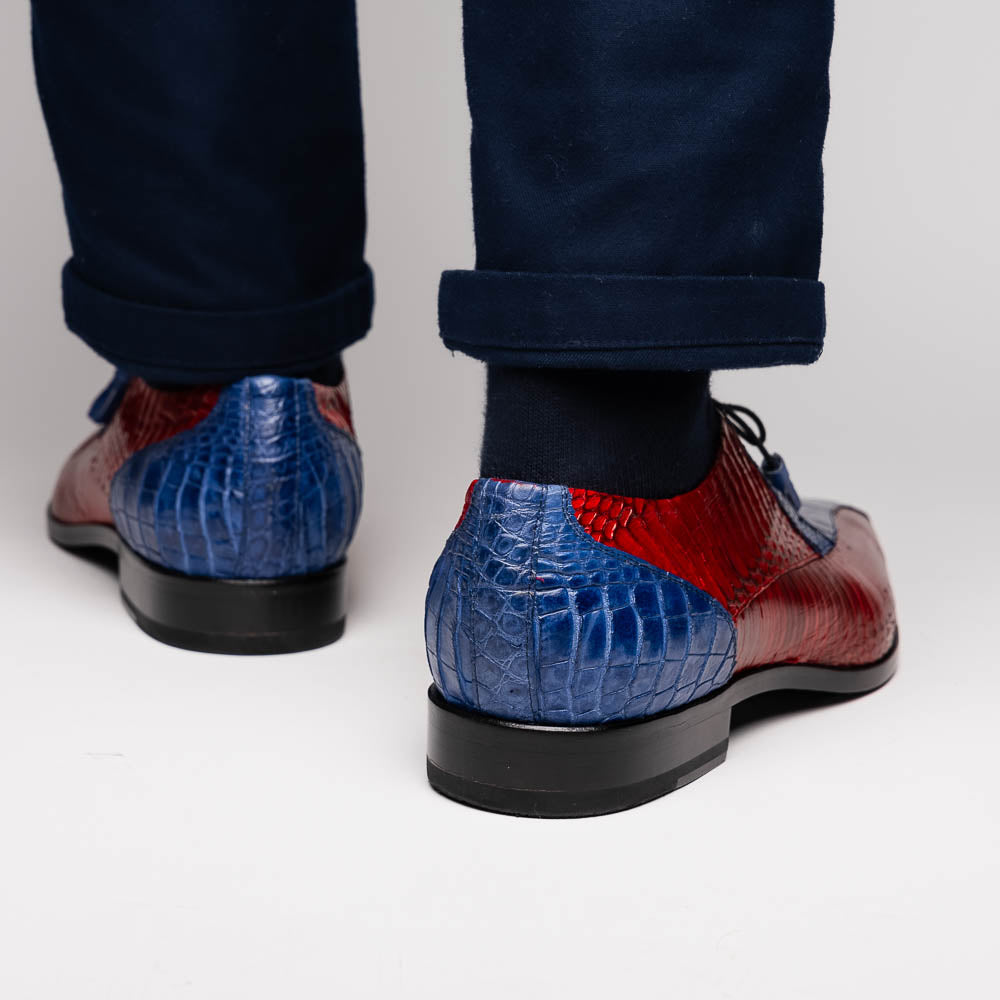 The Moncalieri Navy / Red by Marco Di Milano is a pair of men’s luxury shoes crafted from shiny red and blue crocodile leather with pointed toes, lace-up fronts, hand-painted finishes, and black soles.