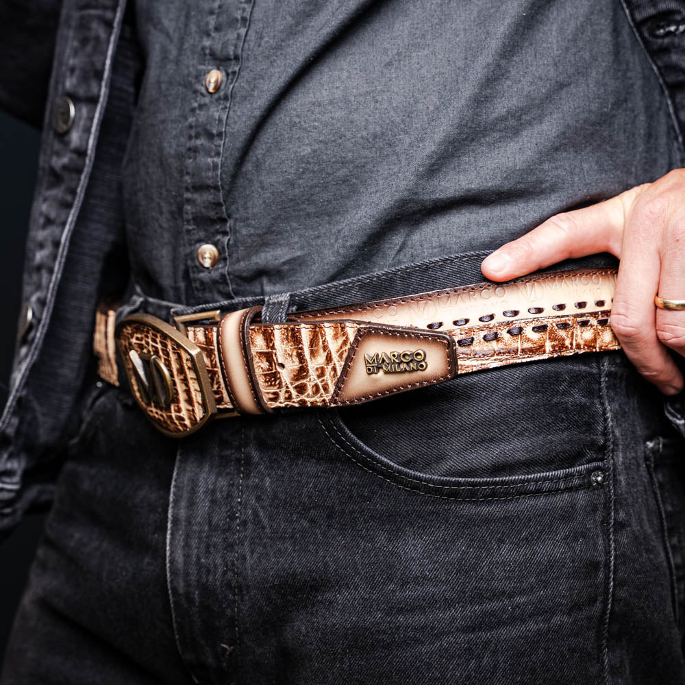 The Montana Belt Stone Orix by Marco Di Milano is a brown handcrafted leather belt with a caiman crocodile pattern and a bold gold MD monogram buckle, elegantly coiled on a white background.