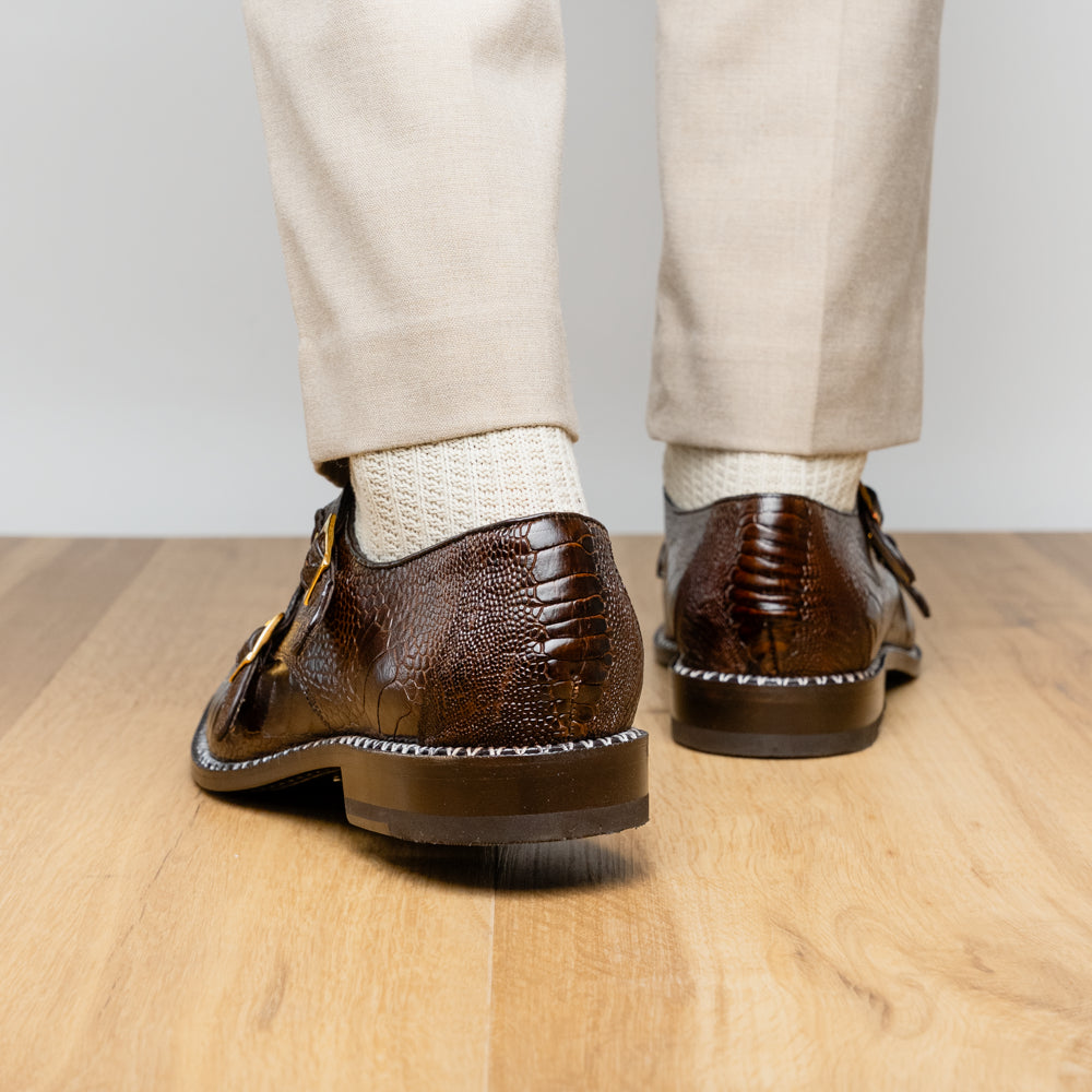 The Marco Di Milano Napoli Brown features brown leather double monk strap dress shoes with a genuine ostrich leg pattern and gold buckles, shown with one shoe upright and the other on its side.