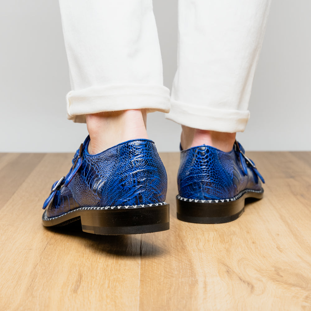 The Marco Di Milano Napoli Electric Blue exotic leather double monk strap shoes are shown: one upright and one on its side displaying the sole, set against a white background.