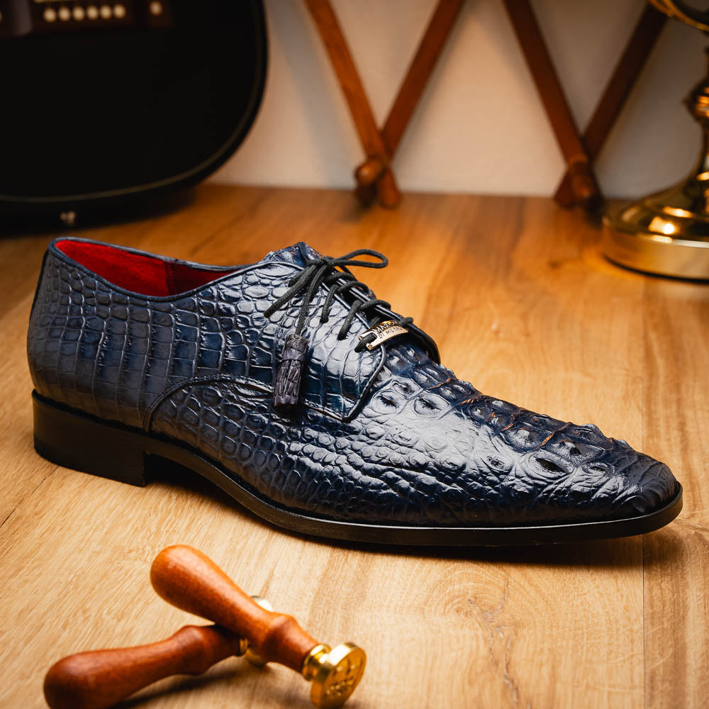 The Nilo Navy by Marco Di Milano features dark blue luxury footwear crafted from premium Nile crocodile skin with black laces and brown leather soles, displayed with one shoe propped on the other.