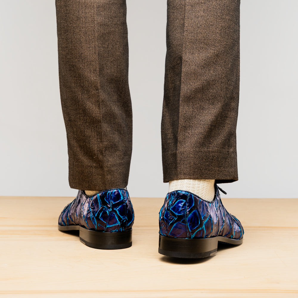 The Olivieri Royal Blue by Marco Di Milano is a pair of men's dress shoes featuring a blue and black textured design. One shoe stands upright, the other displays a bright blue sole with "Marco Di Milano" branding—true luxury.