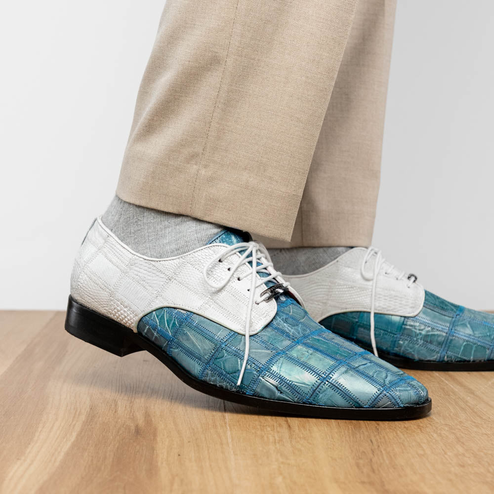 The "Pissa Aqua/White" by Marco Di Milano is a men's dress shoe with a white textured upper, teal blue patterned lower, hand-painted finishes, white laces, and a black sole—showcasing luxury style and craftsmanship.