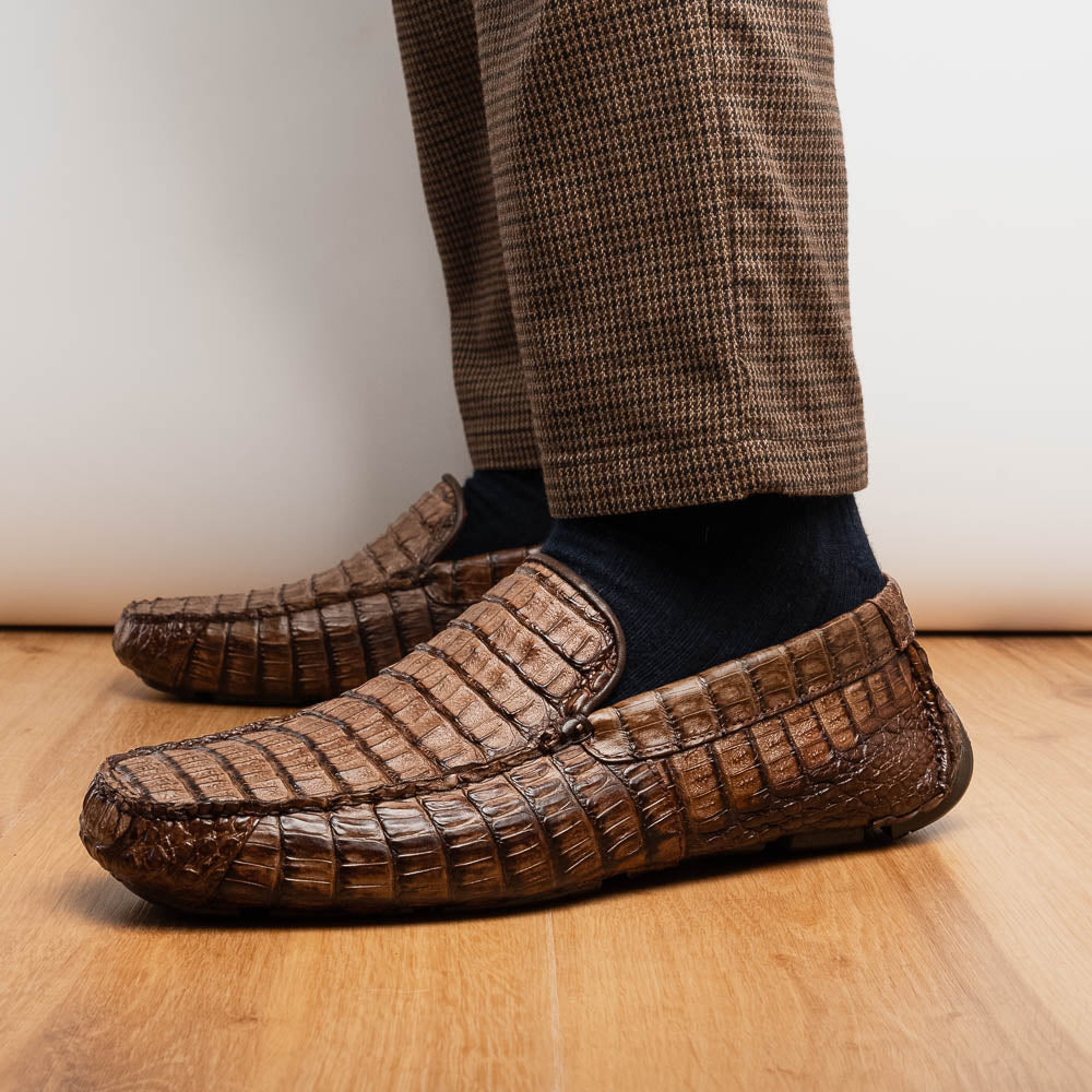 The Remo Washed Brown by Marco Di Milano features luxurious men's loafers with a crocodile texture. One shoe stands upright while the other lies on its side, revealing the detailed sole.