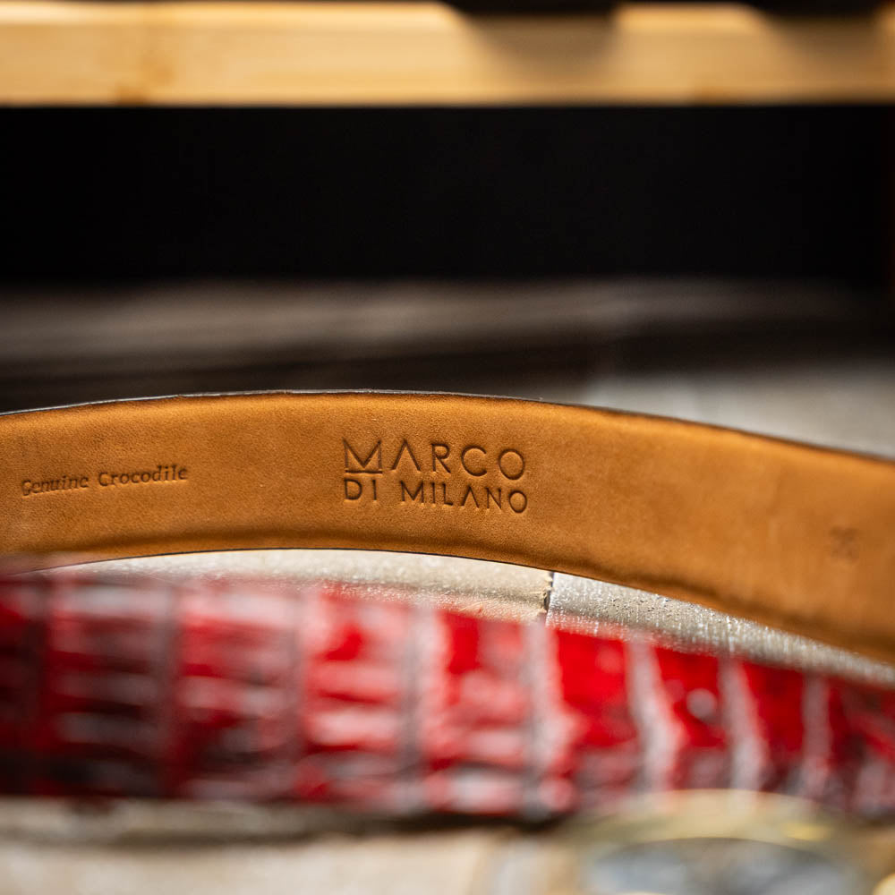 The Riccardo Belt Black Cherry by Marco Di Milano is a genuine caiman fuscus-belly belt in red and black, featuring a silver buckle engraved with the brand’s logo—perfect for lovers of fine exotics.