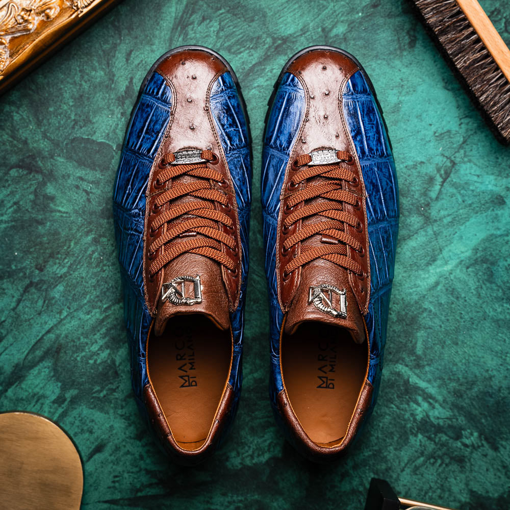 The Marco Di Milano Saulo Blue Jeans is a luxury men's sneaker featuring blue and brown hues, a textured crocodile-like pattern, and a black rubber sole, shown with one shoe upright and the other on its side.