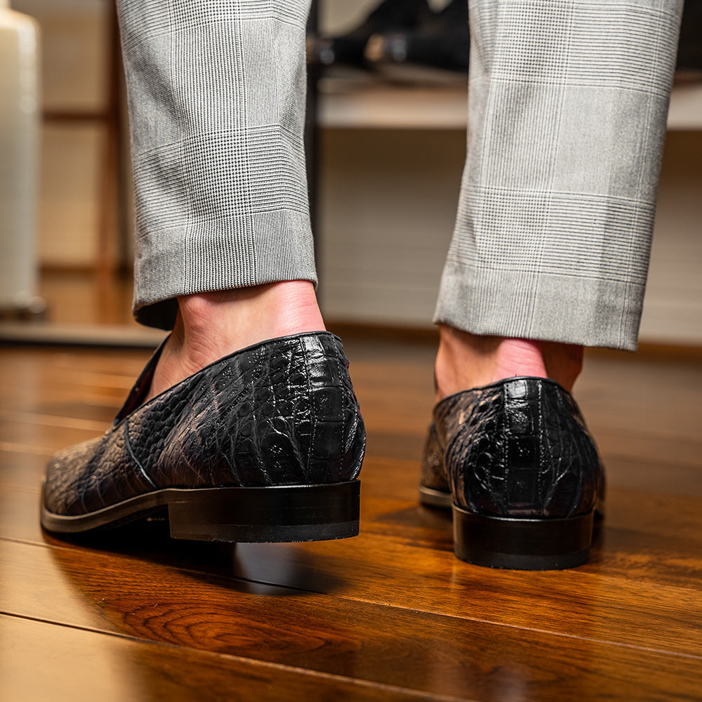 A pair of Marco Di Milano Trento Black loafers crafted from genuine caiman crocodile-pattern leather, showcasing a striking black exterior, red interior lining, and brown soles—one positioned upright and the other on its side. These luxury shoes feature exquisite hand-painted finishes for a truly sophisticated touch.