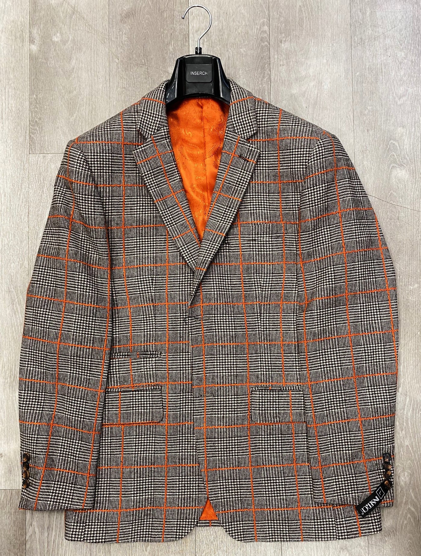 The Inserch Wool Blend Glenn Check Blazer BL002-25 Brown (FINAL SALE, SIZE S ONLY) features an orange lining and orange windowpane pattern, shown on a hanger against a wooden background.