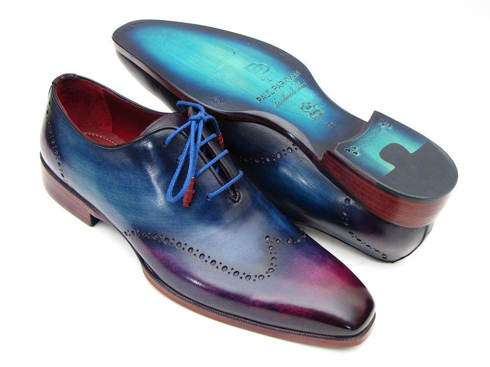 The Paul Parkman Blue & Purple Wingtip Oxfords - 084VX55 are a distinguished pair of men's dress shoes crafted from hand-painted leather with a captivating blue to purple gradient. Featuring blue laces and decorative perforations, these handmade brogues embody a unique blend of style and craftsmanship, making them an elegant choice for the discerning individual.