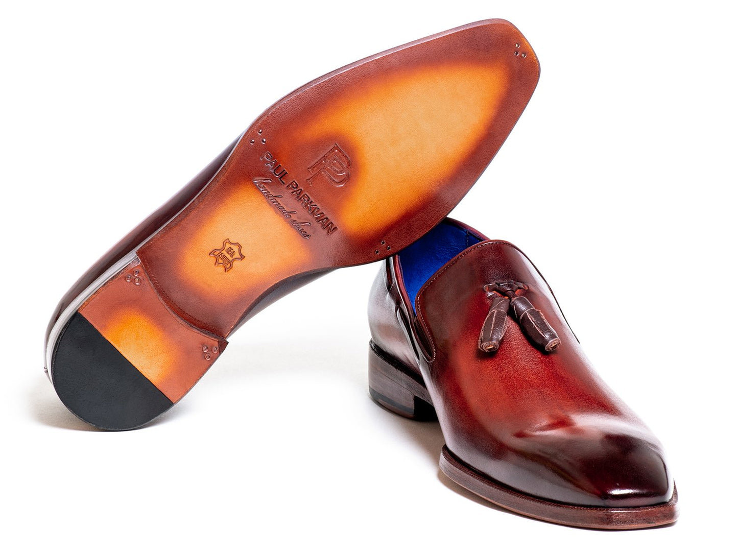 A pair of Paul Parkman Tassel Loafer Garnet Brown - 5141GBRW, featuring polished brown Italian calfskin leather with a sophisticated blue inner lining, stacked elegantly on each other.